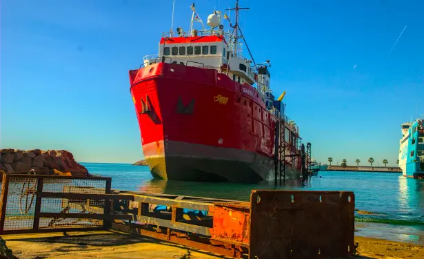 das seenotreetungsschiff seaEye4 wird gerade auf der slipanlage ins trockendock gezogen und der bug kommt aus dem wasser.
im vordergrund ein rostiger haltemast quer auf dem boden