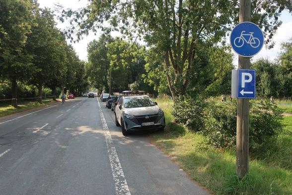 Benutzungspflichtiger Radweg neben einer Straße - von Autos zugeparkt.