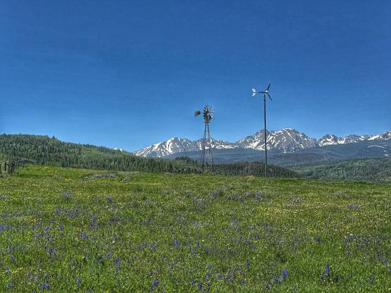 Mountain View landscape in Colorado, with green meadows, flowers, mountains with snow, and windmills.