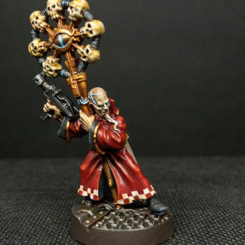 a thin wiry man in long red robes with a staff adorned with many skulls. he has an enormous skull on which several veins pop out