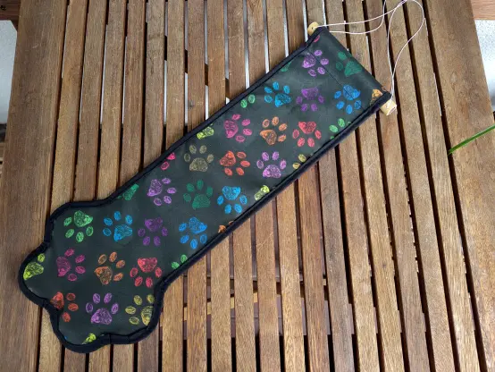 A black banner with colorful paws and black seam lying on a wooden table. It's shaped in the form of a stylized claw and there is thread to hang it somewhere on the top.