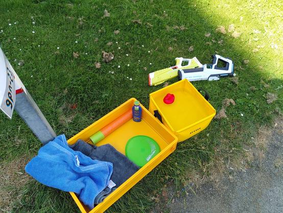 A yellow box with water pistols, some towels and a bucket of water on a smapp patch of grass. It's a sunny day out.