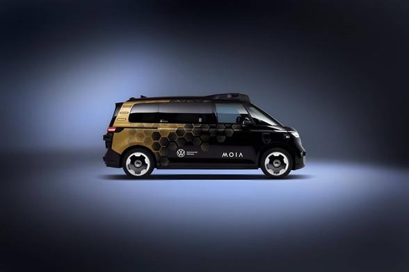 Neuer ID.Buzz AD von Volkswagen und MOIA mit schwarz-goldener Lackierung steht in einem graublau angestrahlten Raum. Foto (c) Volkswagen/MOIA.