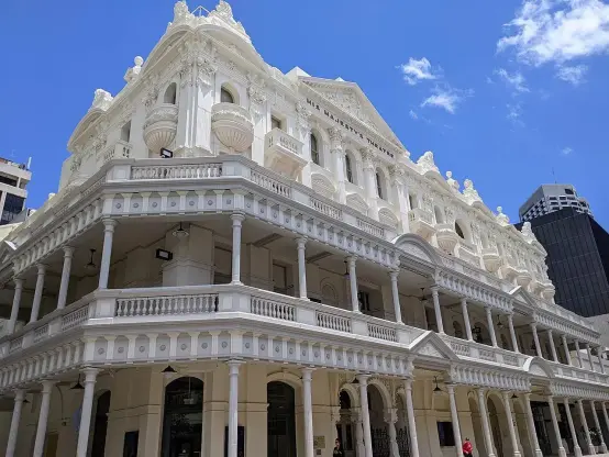 The image depicts a grand, historic building characterized by a white façade, intricate architectural details, and multiple levels. The structure features ornamental elements, including pillars and balconies, set against a bright blue sky with a few clouds. It appears to be an impressive piece of architecture, likely reflecting a classical or colonial style. If you need specific information about the building, feel free to ask!

Image Credits: Wikimedia / The Logical Positivist / CC BY-SA 4.0