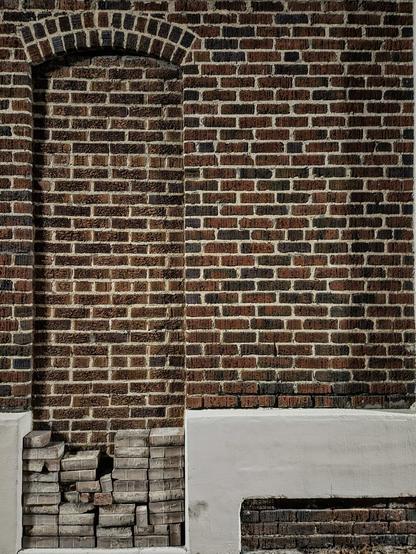 Side of an old crumbling brick building with an indent in the brickwork where there was once a doorway,  now bricked over.