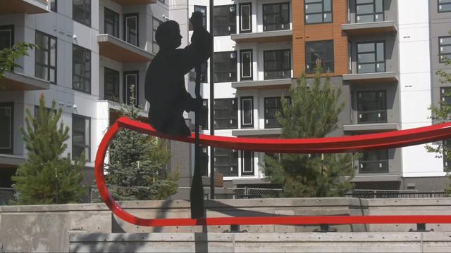 A photo of a steel art sculpture in front of a new residential building. The piece is comprised of a black silhouette of a man paddling, on top of the outline of a canoe in red. (David Mitchell/CTV News Edmonton)