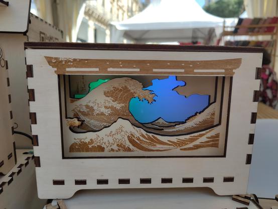 Une boite décorative en bois avec un fond lumineux devant lequel est représentée la Vague de Kanagawa par Hokusai, découpée en trois plaques pour lui donner de la profondeur. La lumière de fond est verte à gauche et bleue à droite