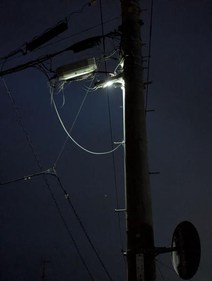 A photo of a power pole at night. There is a light on the other side of the pole so you can only see an outline of the pole and its lines.