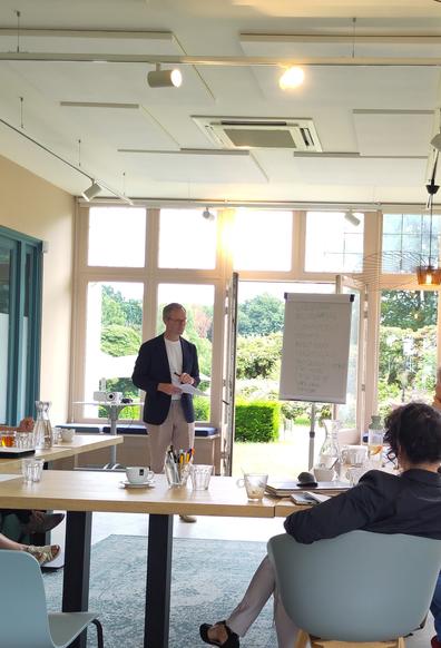 Mijn compagnon die de deelnemers toespreekt, in een ruime serre.