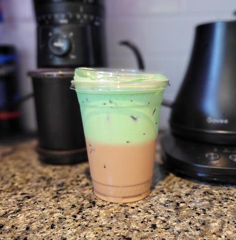 Clear to go coffee cup. The bottom half is light brown coffee, the top is mint green pandan cream.