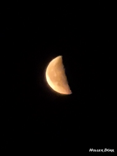 Zunehmender Mond in warmem Licht vor schwarzem Himmel. Die linke Seite ist beleuchtet. Aufnahme bei Nacht, spontan unterwegs entstanden.