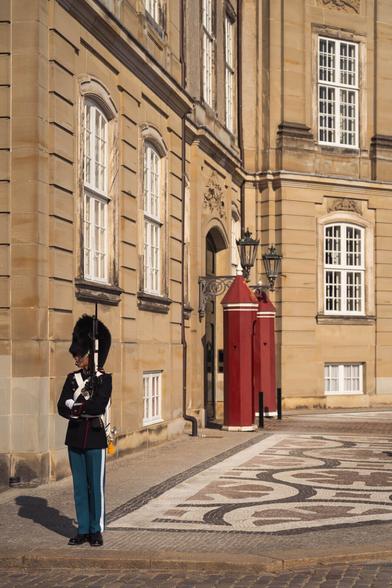 A Royal Danish Guard in traditional uniform standing at attention in front of the historic Amalienborg Palace in Copenhagen, Denmark.