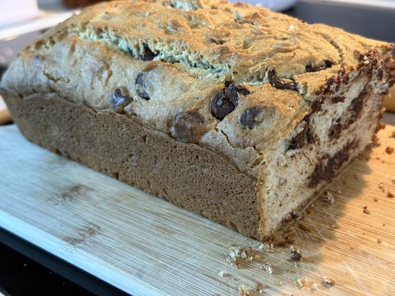 A loaf of light brown banana bread with dark chocolate chips throughout on a wooden cutting board.