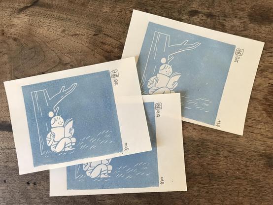 Linocut prints of a character reading a book under a tree. The pictures are printed in clear blue ink.