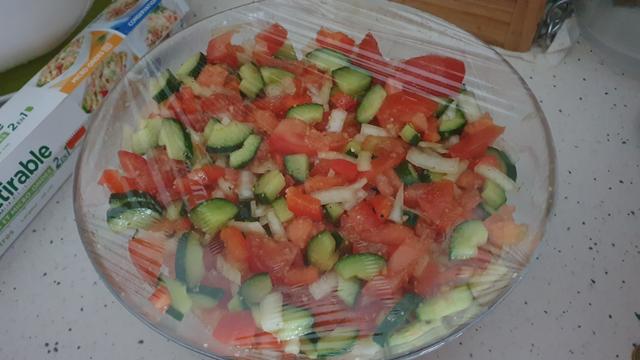Un saladier plein à craquer de dés de tomates, de concombre, de poivron rouge et d'oignon mélangés dans l'huile d'olive et l'ail émincé.