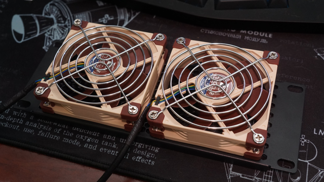 Two Noctua NF-A9 fans mounted to a ventilated 2U plate.  On the fans there are two silver fan grills to prevent my fingers from being sliced.