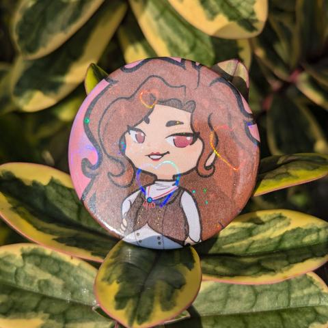 photo of a pinback button badge featuring a drawing of a brunette femme-presenting character in chibi style, with a holographic heart film overlay