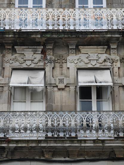The facade of a commercial building with residential upper floors. The balconies are complex, highly detailed works of art with highly stylised nature themes