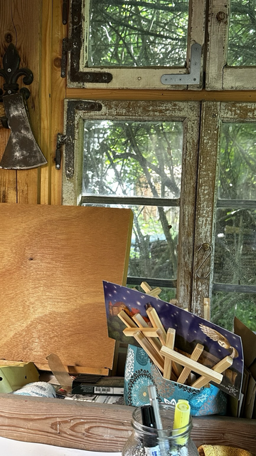 Ein altes Fenster in meinem Gartenatelier. vor dem Fenster steht eine Tischstaffelei. An der Wand hängt eine Axt
