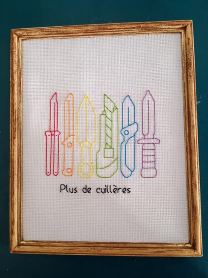 Cadre contenant une broderie représentant 6 couteaux aux couleurs du drapeau LGBT, et légendé "plus de cuillères"