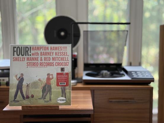 Hampton Hawes - Four! LP cover.

A lot of exclamation points, with the title in black, and the participants in red. Given the pun, four on a golf course, probably yelling "Fore!"

Hey, look, I just describe them.

The black LP plays on a vintage, restored Bang & Olufsen Beogram 8002 linear-tracking turntable to the right.