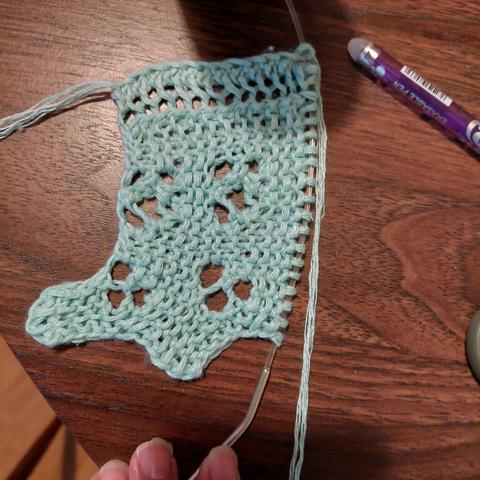 A short sample of a knitted lace edging, looking wonky, on a table top.