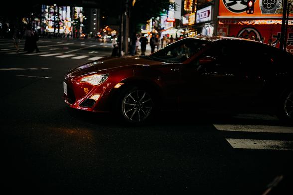 photo of a red tuner car at night at a crossing in Tokyo