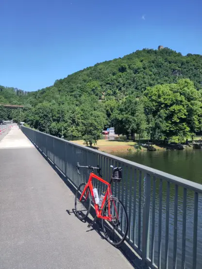 Mein rotes Rennrad lehnt am Geländer der Brücke am östlichen Ende des Hengstey- Sees. Im Hintergrund erhebt sich das Terrain in Richtung Hohensyburg, die vor lauter Grünzeug kaum zu sehen ist.