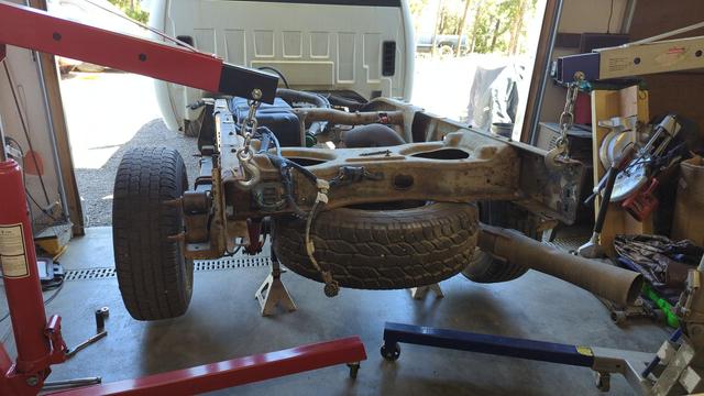 A large truck, partially backed into a garage that's frankly far too small. The rear axle is suspended with jackstands, and further support is provided by two engine hoists attached to the rear frame.