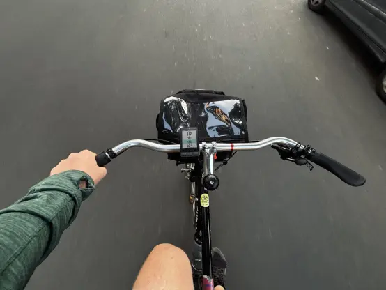 A wide angle photo of the rider’s view while riding with the wide handlebars with a fair bit of backsweep. The left hand is on the handlebar.