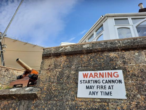 Old wall, cannon, and sign with warning: 'starting cannon may fire at any time'