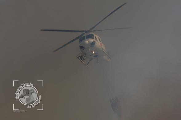 Helicóptero entre una densa humareda realizando una descarga de agua en un incendio