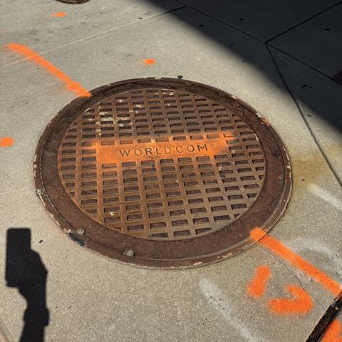 A manhole that says “worldcom” with an orange stripe painted across the words