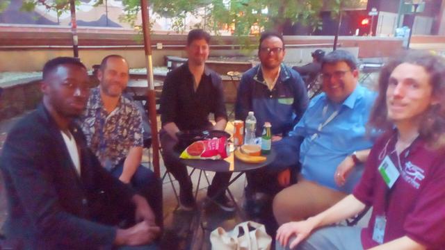 Six men seated outside at public space. Others not in picture. Open Source Week side event