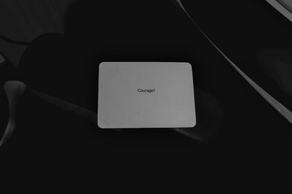 A black-and-white photo of an Oblique Strategy card. The card reads: 'Courage!'.