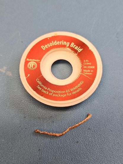 An empty Radio Shack branded desoldering braid package with a short piece of braid sitting next to it.