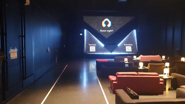 Die Lounge sagt Gold Nicht. Sofas und Tische sind leer. Lampen leuchten noch und die Leinwände sind gemapped. Links und rechts qr codes mit YouTube und Pretalx link