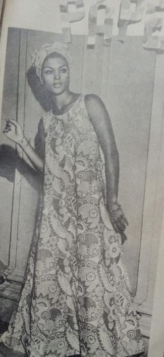 Mujer posando con un vestido estampado de papel en un ambiente retro, con un fondo que sugiere un estilo de los años 60.