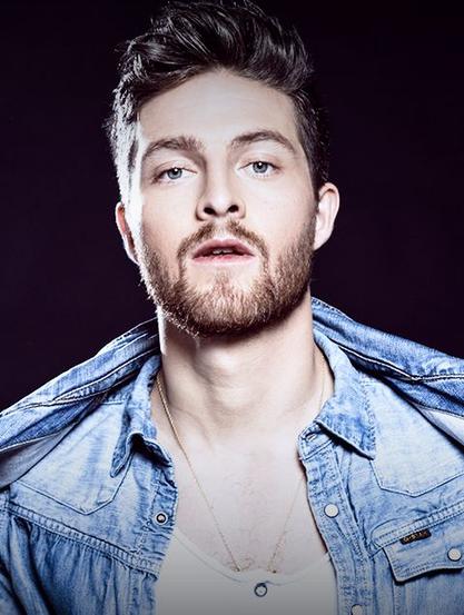 Retrato de un Eddy Villard, vistiendo una chaqueta de mezclilla sobre una camiseta blanca, con expresión neutral frente a un fondo oscuro.