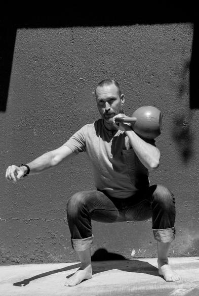 A black and white photo of a man squatting with a kettlebell