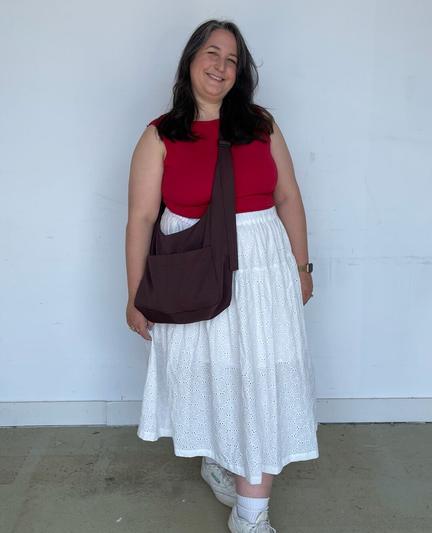Caroline wears a red boatneck tank, white eyelet skirt, and a brown messenger bag with white socks and sneakers.