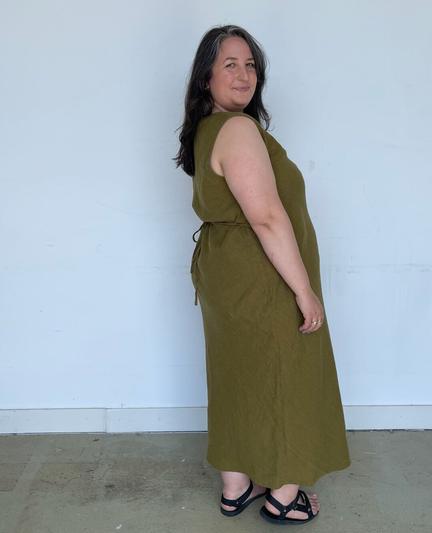 Caroline wears a long green bias-cut linen dress with a tie at the back waist and sandals.