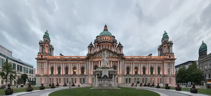 This image depicts the Belfast City Hall, located in Belfast, Northern Ireland. It is an iconic building known for its impressive architecture, including a large dome, ornate detailing, and green copper roofs. The building is surrounded by gardens and is often a site for public gatherings and events. The sky appears cloudy, giving a dramatic backdrop to the structure.

Image Credits: Wikimedia / Giorgio Galeotti / CC BY 4.0