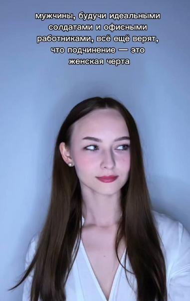 Фотография по грудь белой темноволосой девушки с волосами ниже плеч, свисающих по обе стороны, и открывающих правое (левое для наблюдателя) ухо с белой маленькой серьгой. Губы девушки накрашены красным, на щёки нанесены румяна. На девушке надета белая одежда типа рубашки, но с небольшим декольте. Девушка смотрит влево (вправо для наблюдателя) и легко улыбается. Девушка стоит на белом фоне. Подпись: «Мужчины, будучи идеальными солдатами и офисными работниками, всё ещё верят, что подчинение — это женская черта.»