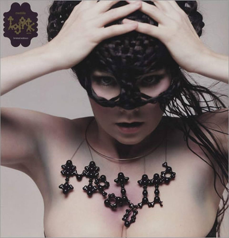 A picture of Björk looking right through the camera, with her hands on her head, with a big necklace where "Medulla" is written with black round shapes. She's also wearing a mask made of breaded hair.
