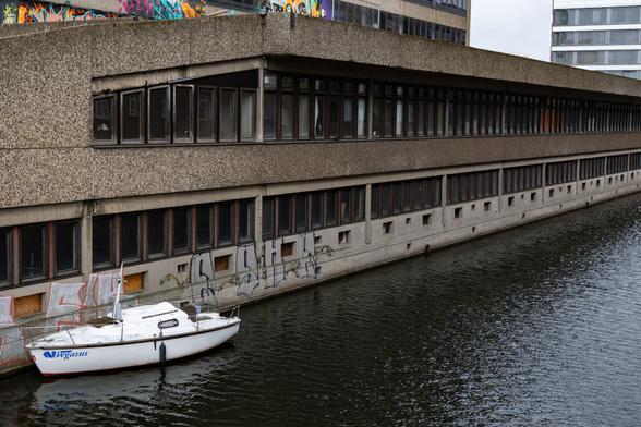 Color photo of a modern sailboat (without a mast) moored in an urban canal.