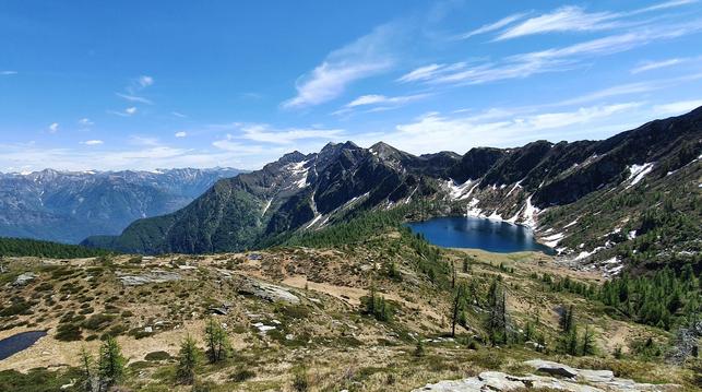 Foto einer Berglandschaft. Im Vordergrund ein Plateau mit einem Bergsee umgeben von Bergen, links ein tiefes Tal, hinten eine Bergkette