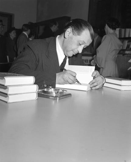 US-Information Center in Wien 1., Kärntnerstraße 38.: Friedrich Torberg in Anzug und Krawatte signiert sitzend sein Buch Die zweite Begegnung. Am 19. April 1951. Nachweis von wiki commons folgt.