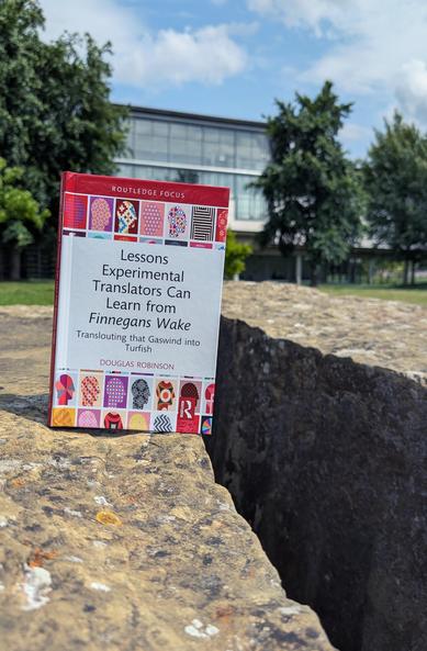 Robinson's book "Lessons Experimental Translators Can Learn from Finnegan's Wake" balanced on the edge of a large stone in front of SUB library, next to which, after a sizable gap, looms another big stone