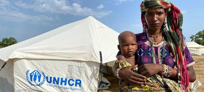 Une femme et son enfant devant une tente du UNHCR à El Radoum (Darfour du Sud, Soudan) en 2022 (photo © UNHCR/Behrooz Taleb)